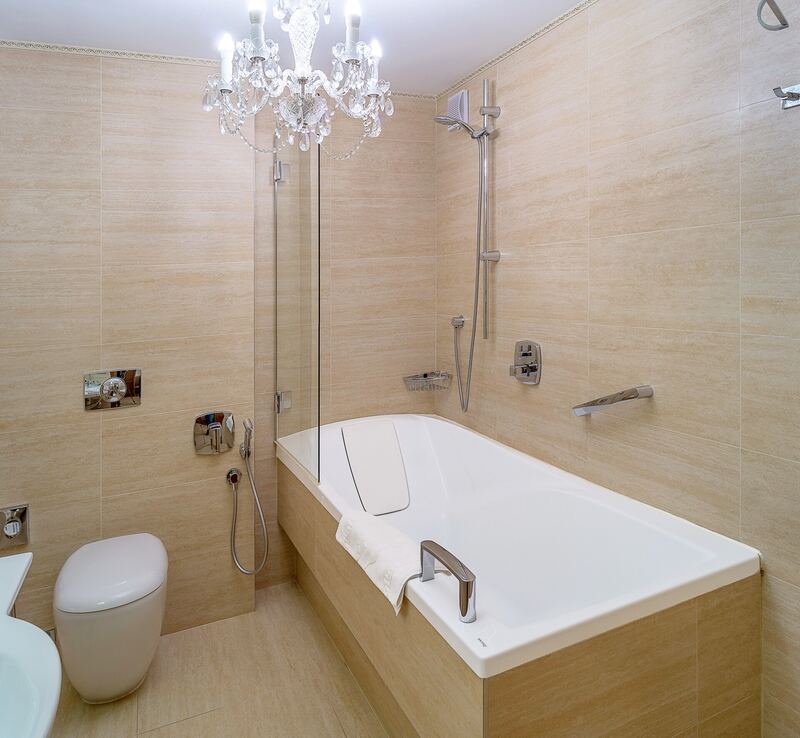 Bathroom with beige stone-effect tiles, a built-in bath and a glass shower screen