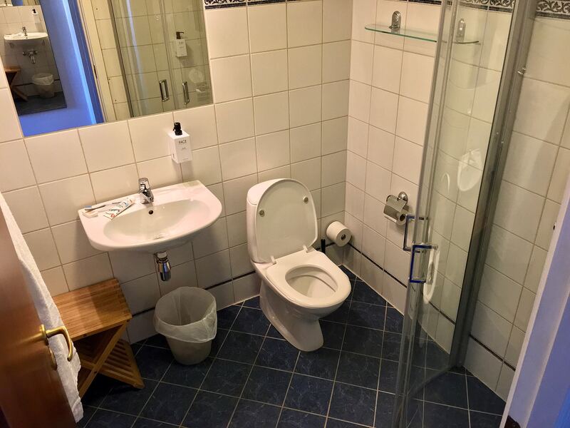 Compact bathroom with white wall tiles, dark floor tiles, a basin and mirror and a corner shower