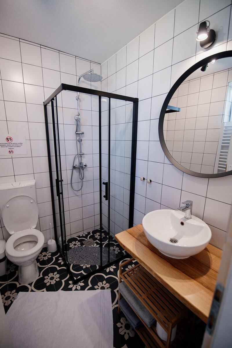 Small shower room with a black-framed shower enclosure, round mirror, basin on a timber shelf and patterned floor tiles
