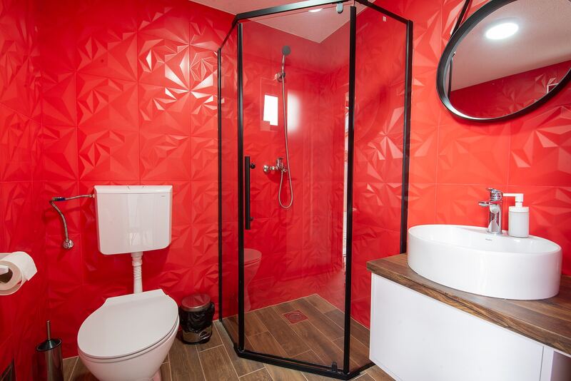 Bathroom with bright red patterned wall tiles, a glass shower, a round mirror and white basin