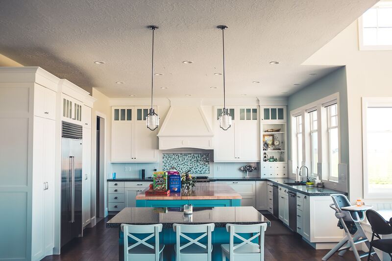 Kitchen with a blue island, white cabinets, stools and pendant lights