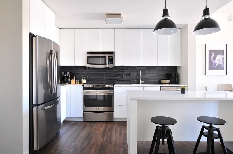 White kitchen with a breakfast bar, two stools and black pendant lights